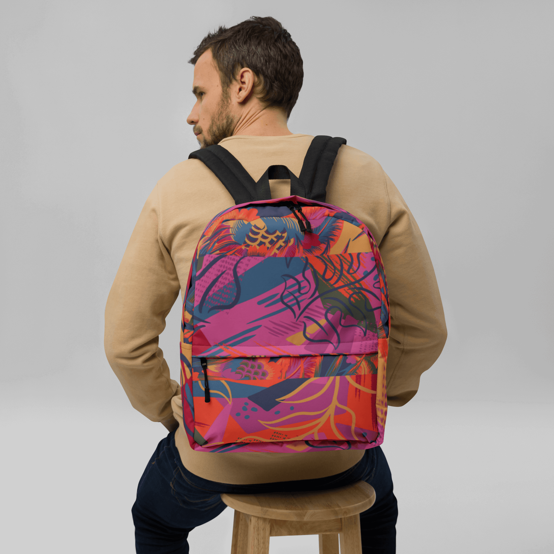 FLORES - Mochila URBAN Unisex - Hombre con mochila colorida y estampado floral desde atrás sobre una silla.