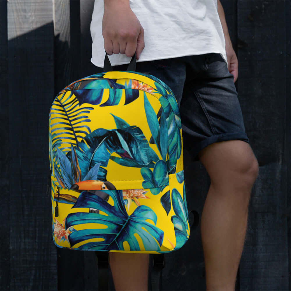MOCHILA TUKAN URBAN UNISEX en diseño tropical con hojas verdes y fondo amarillo, ideal para estilo streetwear.